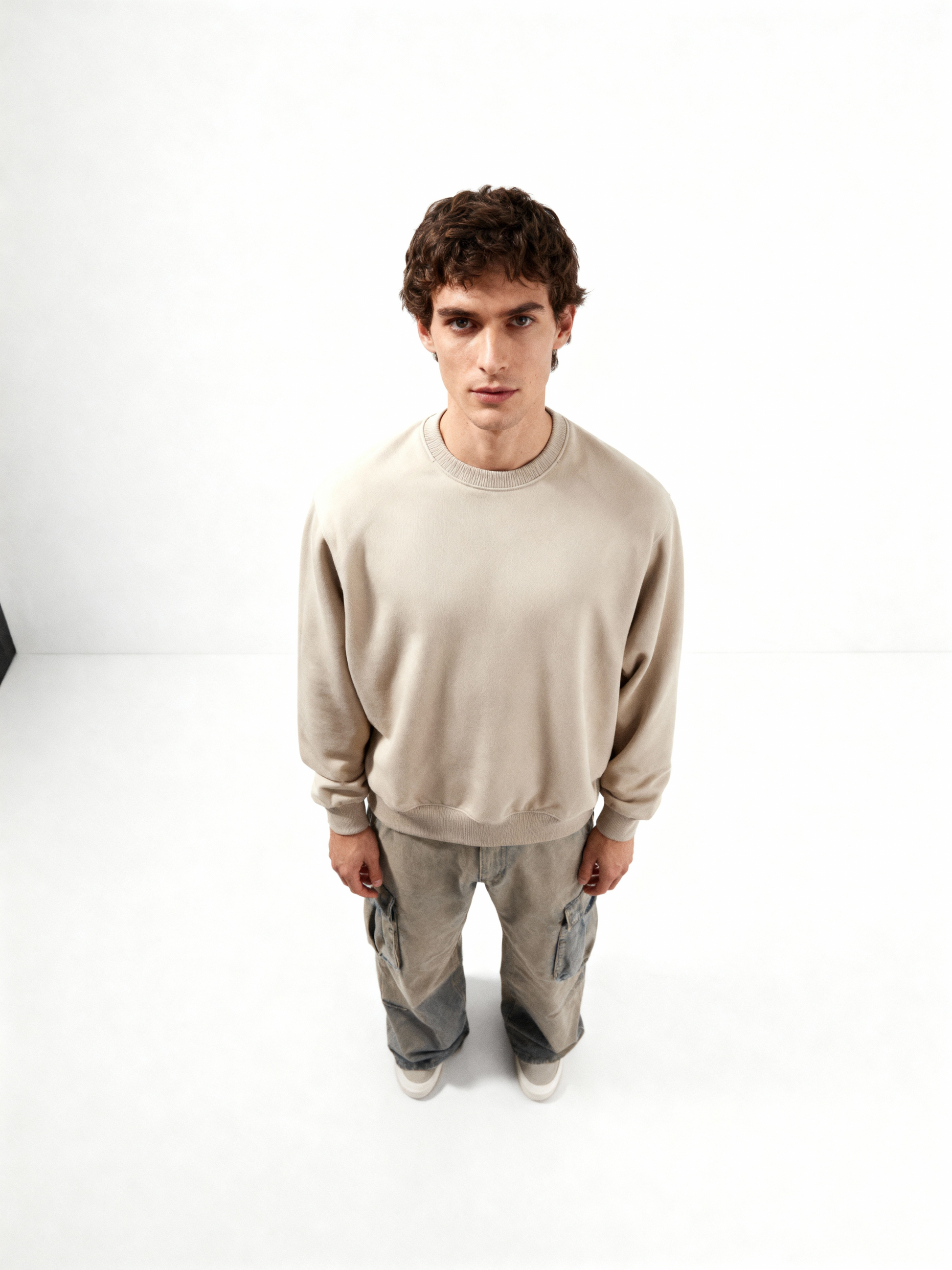Man wearing a beige sweatshirt and gray pants on a white background