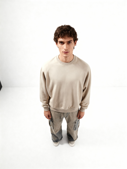 Man wearing a beige sweatshirt and gray pants on a white background