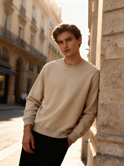 Man wearing a beige sweater leaning against a stone wall in an urban setting