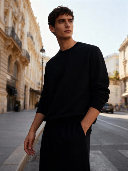 Man wearing a black sweater and pants standing on a city street.