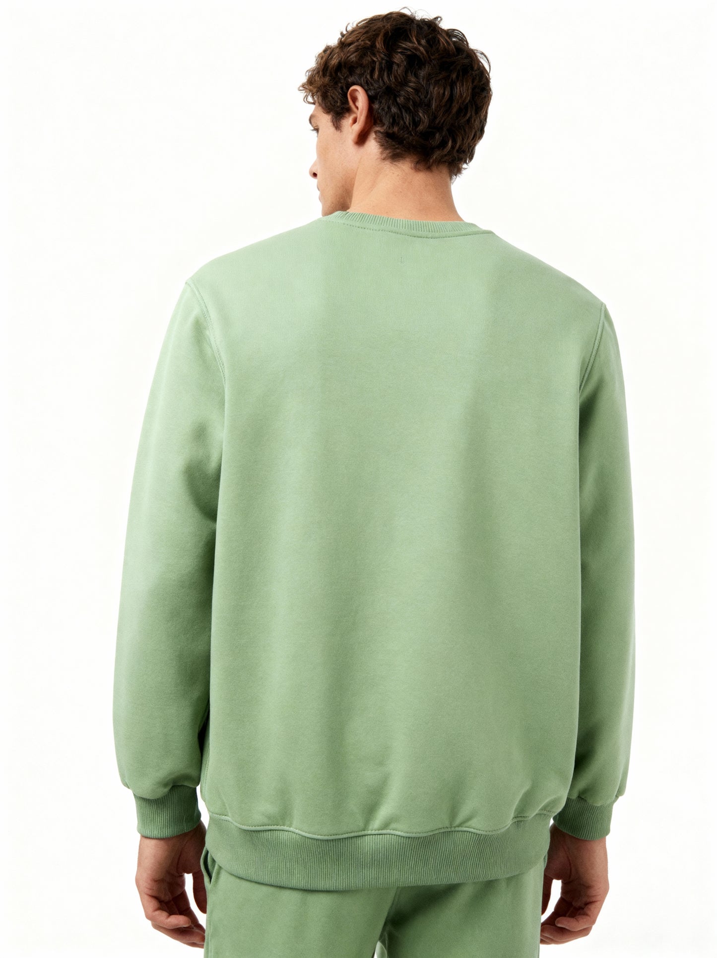 Person wearing a green sweatshirt and pants on a white background