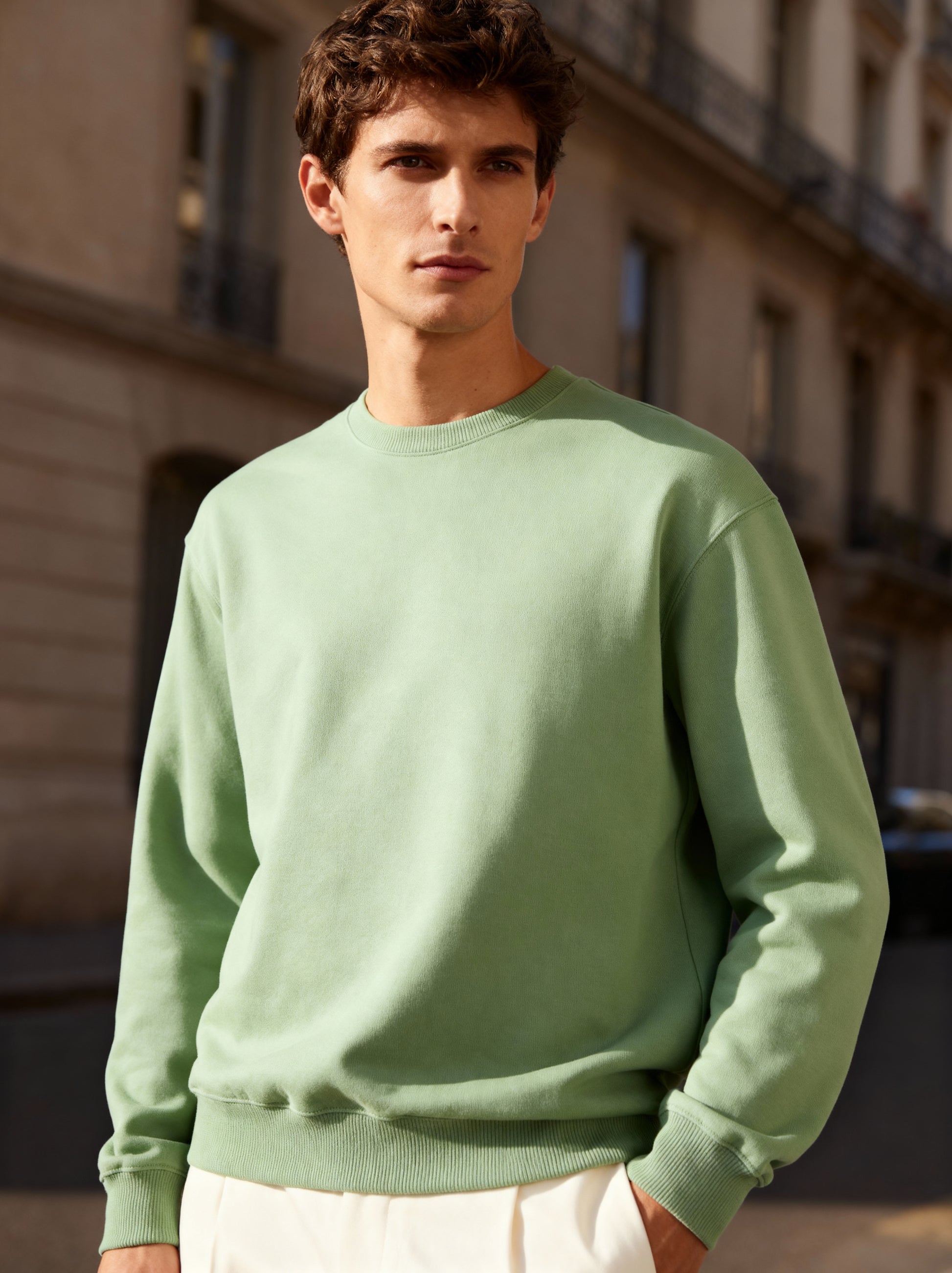 Man wearing a light green sweatshirt standing in an urban setting