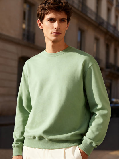 Man wearing a light green sweatshirt standing in an urban setting