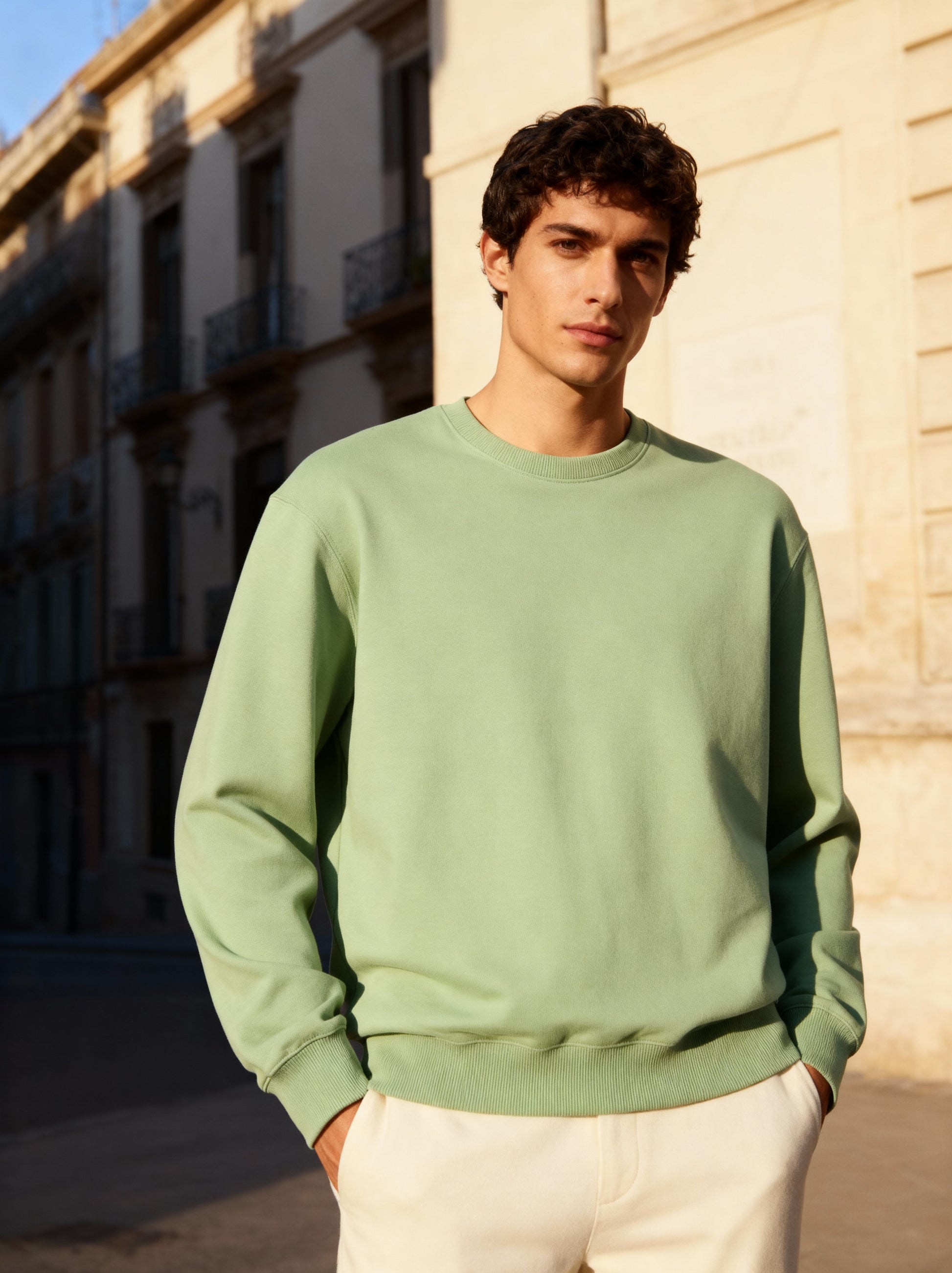 Man wearing a light green sweater standing against a building.