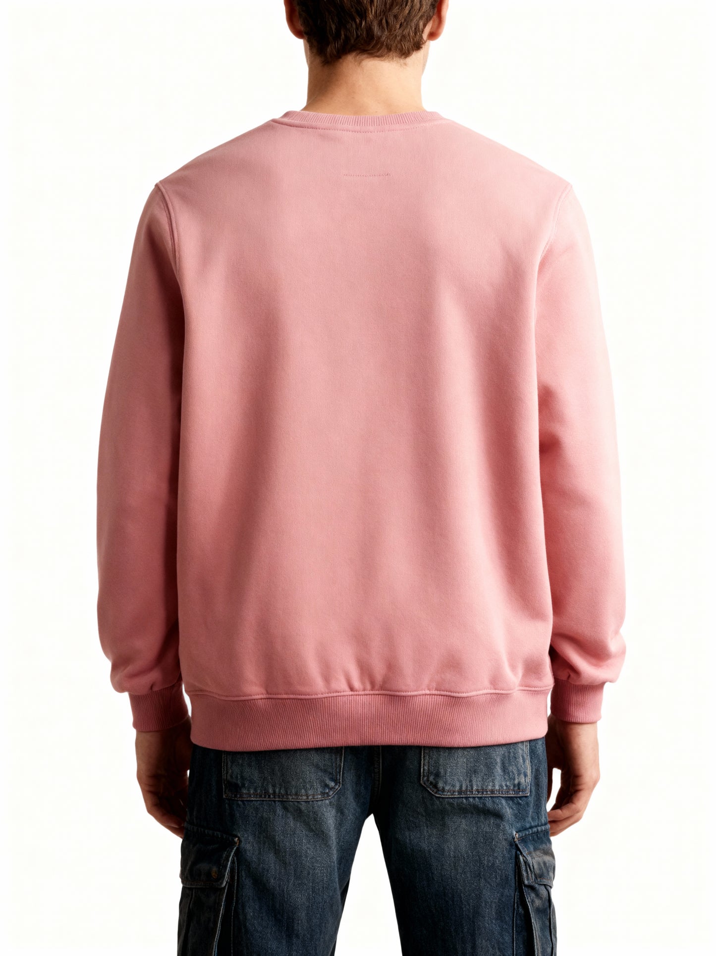 Person wearing a pink sweatshirt and dark jeans on a white background