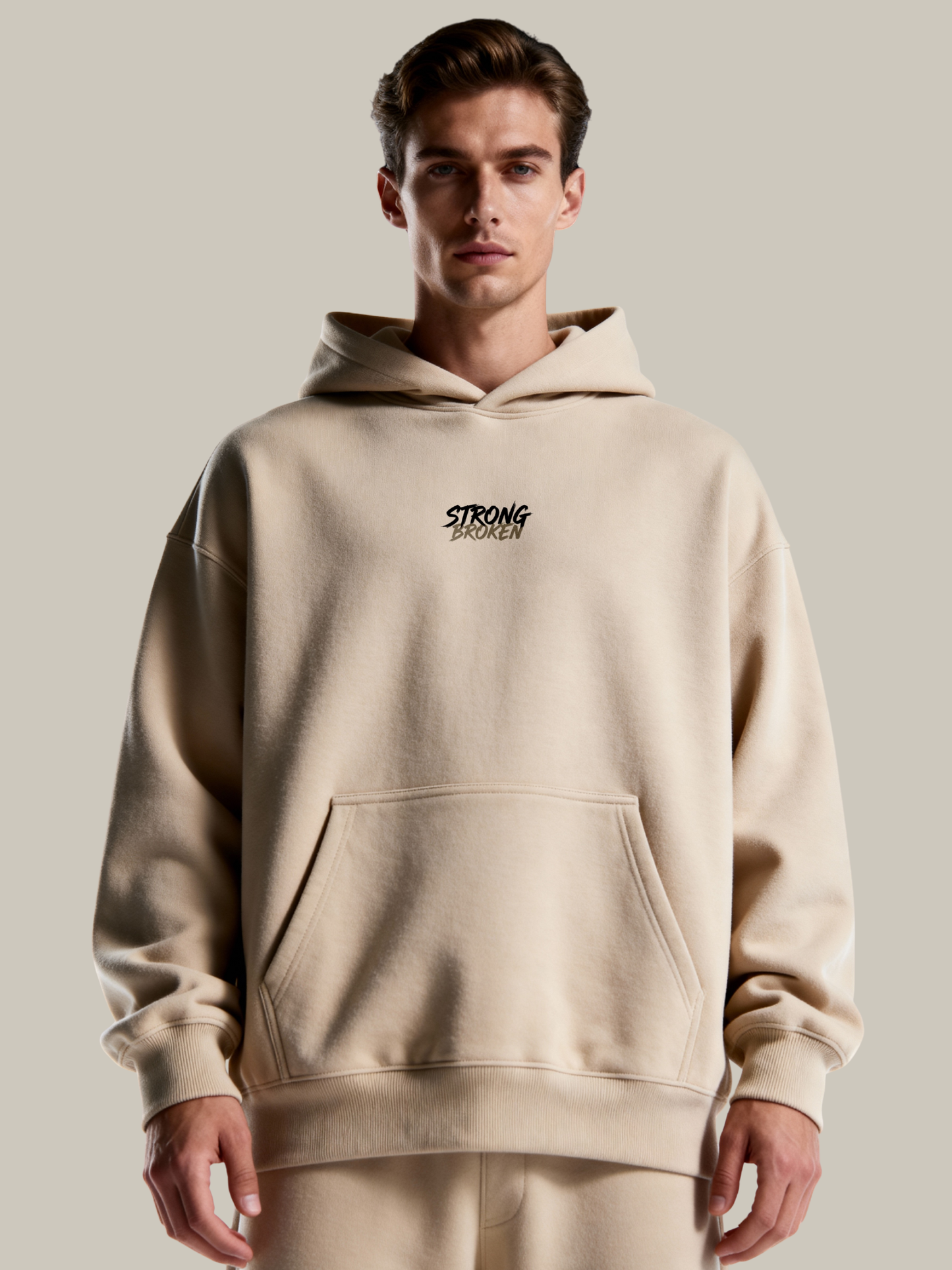 Man wearing a beige hoodie with 'STRONG' branding on a plain background