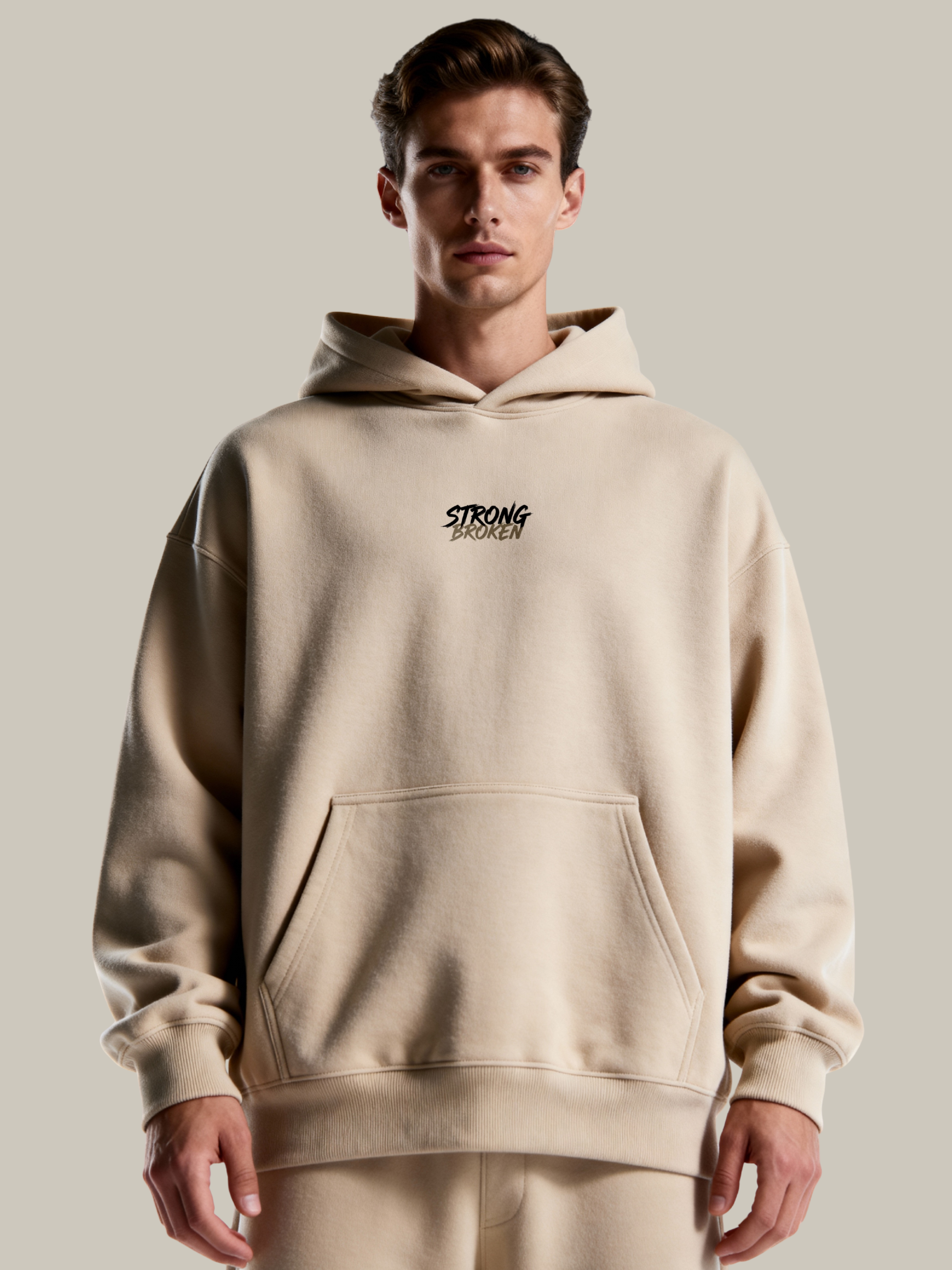 Man wearing a beige hoodie with 'STRONG' branding on a plain background