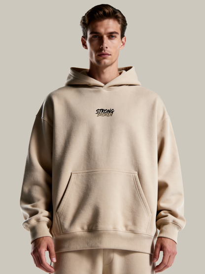 Man wearing a beige hoodie with 'STRONG' branding on a plain background
